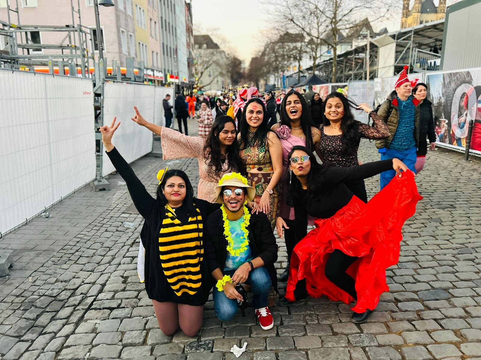 A group of friends in colorful Cologne Carnival costumes posing on a cobblestone street.